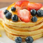 Stack of fluffy cherry ricotta pancakes with maple syrup