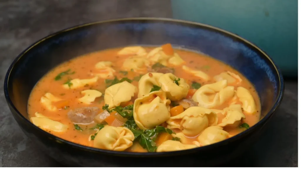 Bowl of sausage tortellini soup with bread and spoon for serving
