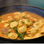 Bowl of sausage tortellini soup with bread and spoon for serving