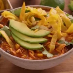 Bowl of chicken tortilla soup garnished with avocado, tortilla strips, and cilantro